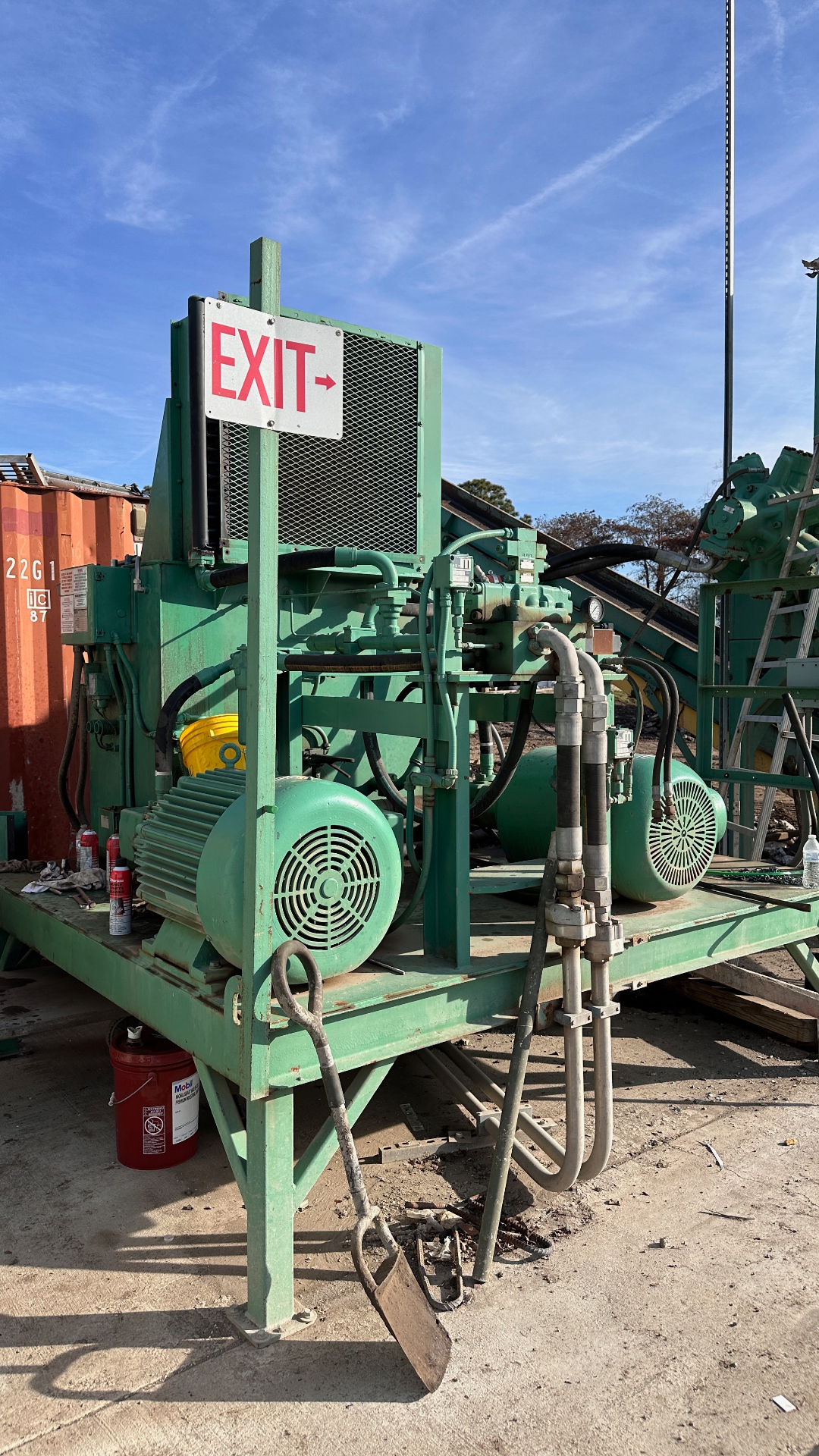 Close-up of the green hydraulic two-ram baler power pack with twin electric motors, hydraulic lines, and pressure gauges under a clear blue sky