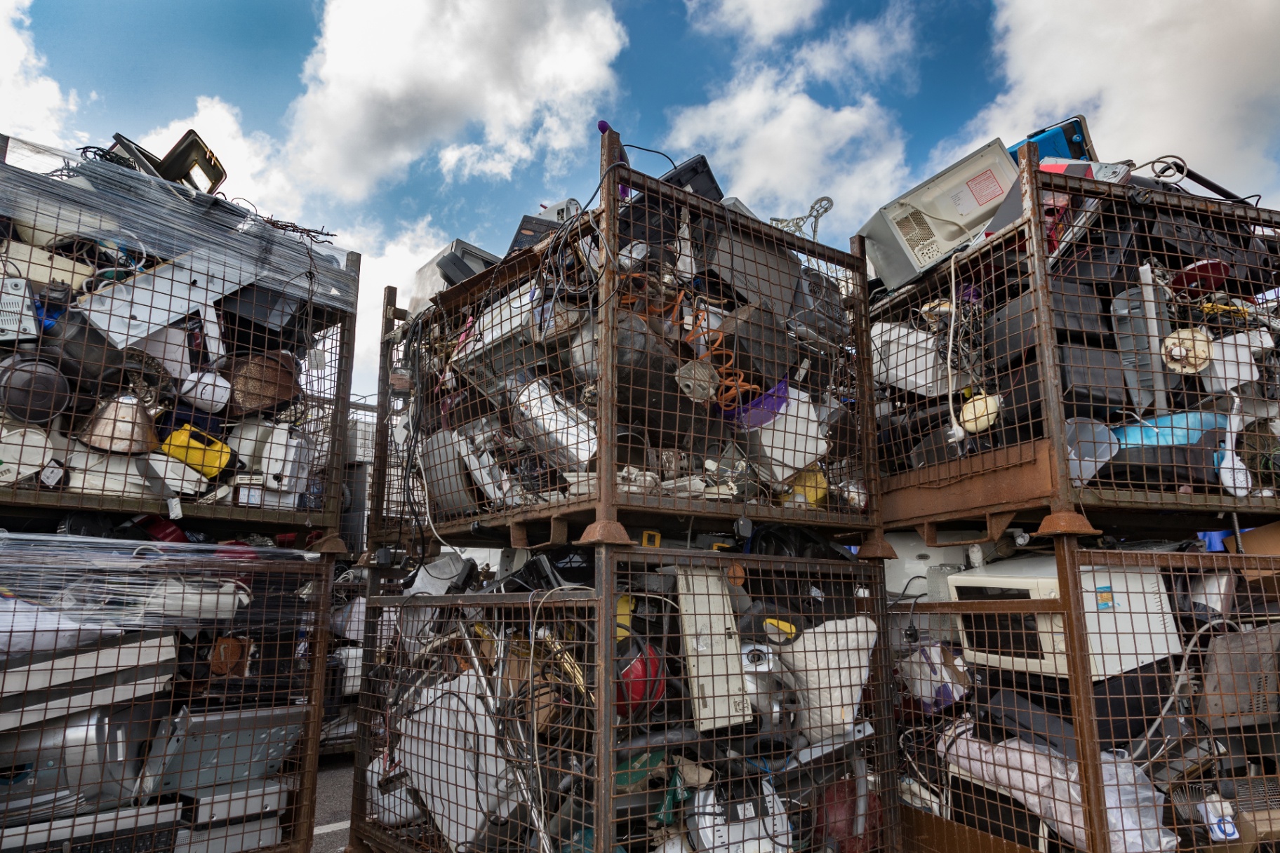 Wire cages stacked with e-scrap — CPUs, boards, and mixed electronics — on a warehouse floor